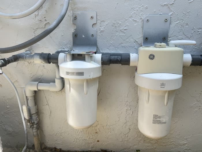 Two-stage whole-home water filtration system mounted on an exterior wall